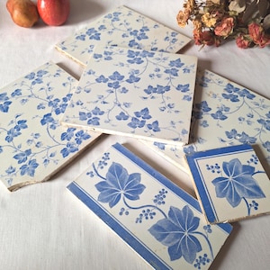 May include: A selection of vintage square tiles, predominantly white with blue floral patterns. The tiles display a repeating design of blue ivy leaves and vines. Some tiles have a border with large blue leaves.