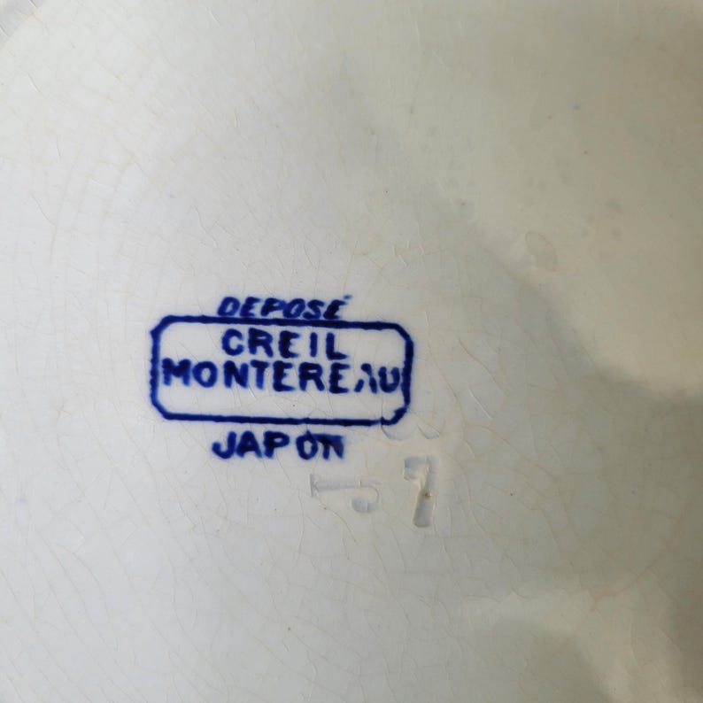 May include: A blue and white ceramic stamp with the text "DEPOSE CREIL MONTEREAU JAPON" in a rectangular frame.