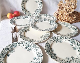 May include: A set of eight white ceramic dinner plates with a green floral design. The plates have a scalloped edge and a raised rim.