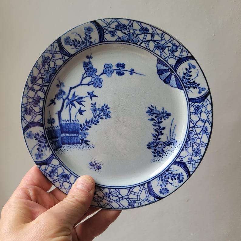 May include: A blue and white porcelain plate with a floral design. The plate has a delicate blue and white pattern with a floral motif and a lattice border.