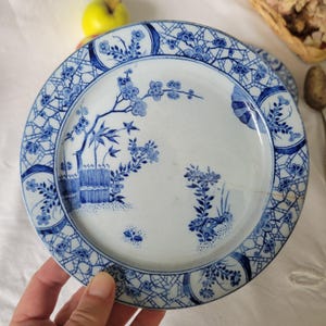 May include: A white ceramic plate with a blue and white floral design. The plate has a scalloped edge and a raised rim.