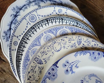 Op de afbeelding: Een stapel van vijf keramische borden met diverse blauw-witte transferware patronen. De ontwerpen bevatten florale motieven, geometrische randen, krulwerk en gedetailleerde filigraanpatronen op witte achtergronden met golvende of gladde randen.