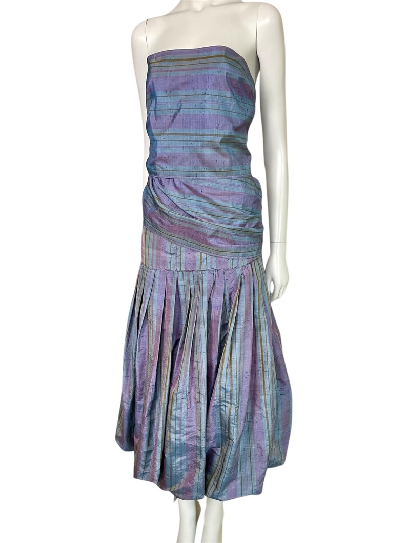 Może przedstawiać: Sukienka bez ramiączek w pasy w kolorze fioletowym i niebieskim. Sukienka ma dopasowany gorset i pełną sp&oacute;dnicę.