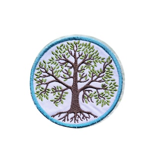Pode incluir: Um emblema bordado circular apresentando uma árvore castanha com folhas verdes e raízes visíveis sobre um fundo branco, rodeado por uma borda costurada em azul claro. O design está centrado dentro da forma redonda de tecido.