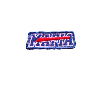 May include: Embroidered patch with the word "MATTA" in white letters on a blue background, with a red horizontal stripe through the center. The patch has a blue border and is rectangular in shape.