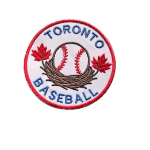 May include: Embroidered patch with a baseball in a nest, flanked by red maple leaves. The patch has a red border and the words "TORONTO BASEBALL" in blue. The baseball is white with red stitching.