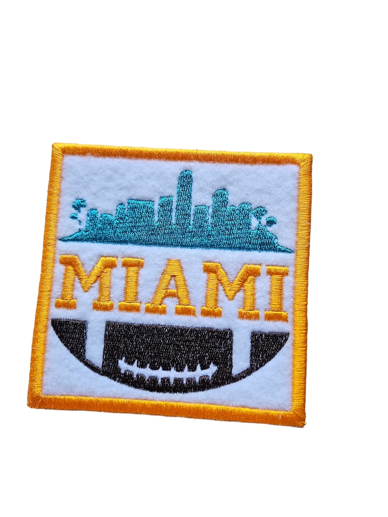 May include: An orange embroidered patch with a white background. The patch features a blue silhouette of the Miami skyline and the word "MIAMI" in yellow letters. A black and white football is below the skyline.