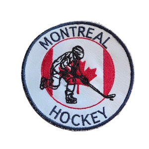 May include: Embroidered patch featuring a hockey player in red and black, set against a Canadian flag design. The patch is circular, with the words "MONTREAL" and "HOCKEY" in a blue font, and a black border.