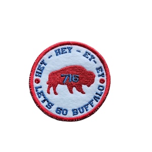 以下が含まれることがあります： 白のバイソンのシルエットと「Hey - Ex - Hey Let's Go Buffalo 716」の文字が刺繍された赤と青のワッペン。