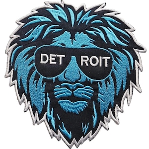 Puede incluir: Un parche bordado azul y negro de un león con gafas de sol con la palabra "DETROIT" escrita en las gafas.