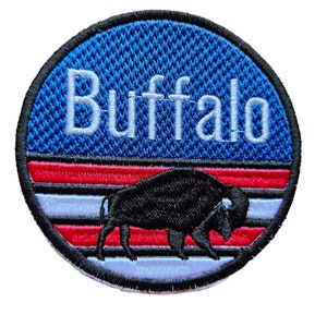 May include: Circular embroidered patch with the word "Buffalo" in white lettering above a black bison. The patch has a blue textured background, with red and white stripes below the text, and a black border.