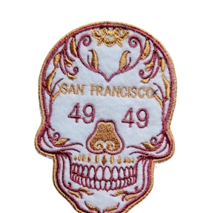 May include: White embroidered patch with a red outline of a skull with gold details. The skull has a floral design around the top and the text "SAN FRANCISCO" and "49 49" inside.