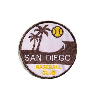 May include: A circular patch featuring the text "SAN DIEGO BASEBALL CLUB". The patch has a white background with a brown wave and palm trees. A yellow baseball is also featured in the design. The patch is bordered with brown stitching.