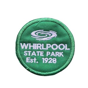 May include: A circular green embroidered patch featuring a white stylized swirl graphic at the top. Below the graphic, the white text reads WHIRLPOOL STATE PARK and Est. 1928. The patch has a stitched green border around the entire circumference.