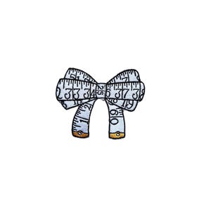 May include: A white measuring tape shaped into a bow with black numbers and gold accents.