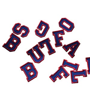 May include: A collection of blue and red embroidered patches spelling out "BUFFALO". The patches are in a collegiate style, with a blue background and red trim. The letters are scattered across a white background.