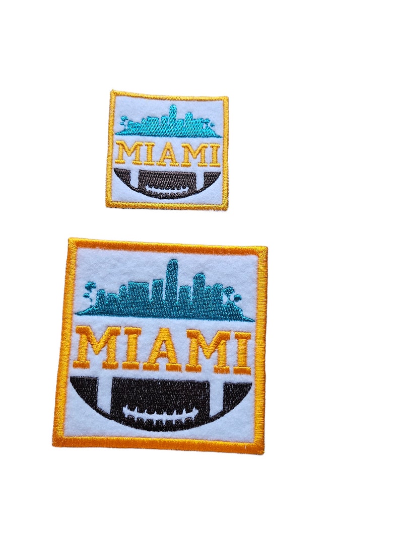 May include: Two embroidered patches with a white background, a gold outline, and a black and white football graphic. The top patch is smaller and features a teal skyline with the word "MIAMI" in yellow. The bottom patch is larger and features a teal skyline with the word "MIAMI" in yellow.