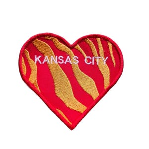 May include: A heart-shaped patch with a red background and gold tiger stripe design. The words "KANSAS CITY" are embroidered in white across the center. The patch has a red border.
