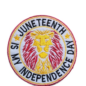 May include: A circular patch with the text "Juneteenth Independence Day" in black, surrounding a lion's head. The lion is yellow and red, with yellow stars on either side. The patch has a white background and a red border.