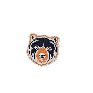 May include: An embroidered patch featuring a black bear head with orange details. The bear's face is detailed with a black nose and white teeth.