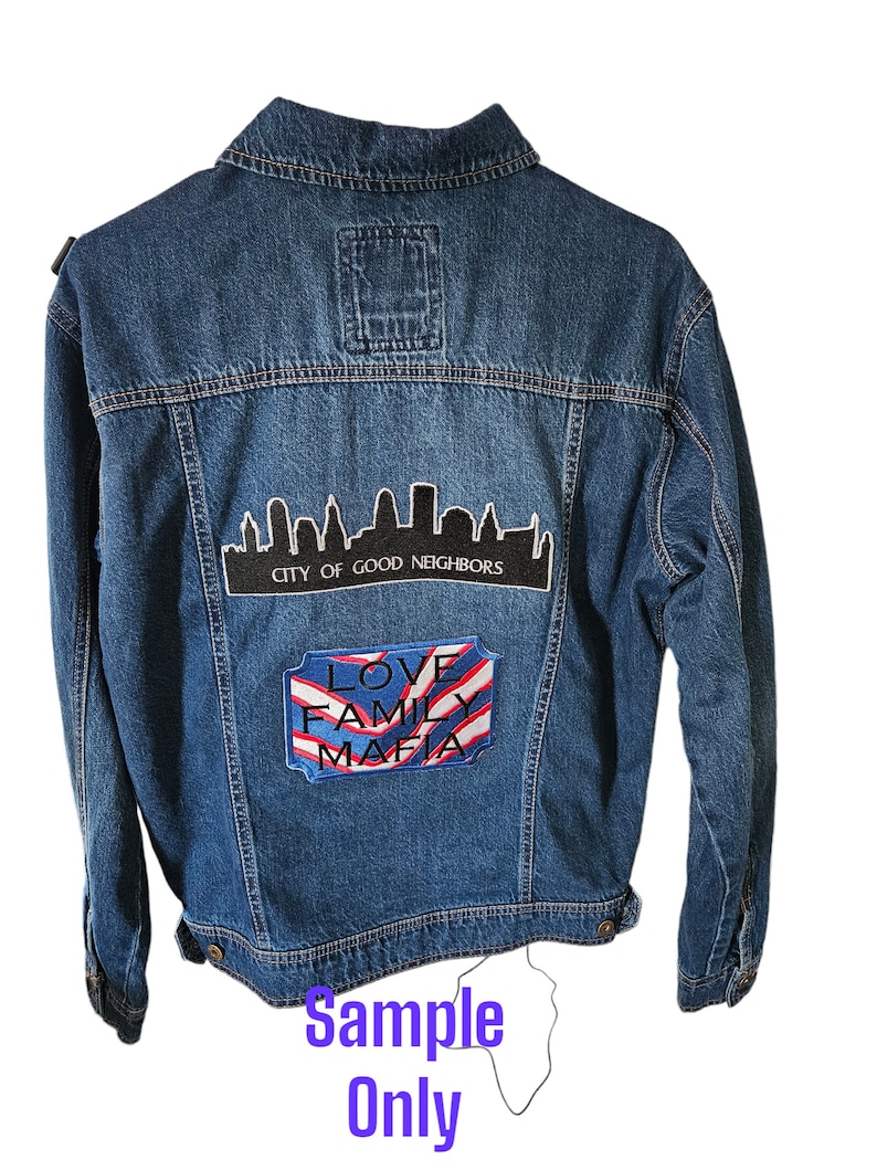 May include: A blue denim jacket with patches. One patch features a city skyline with the text "CITY OF GOOD NEIGHBORS." Another patch displays "LOVE FAMILY MAFIA" with red and white stripes. The text "Sample Only" is at the bottom.