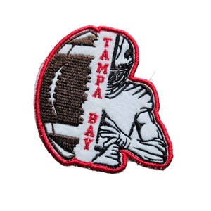 May include: A red, white, and black embroidered patch with a football player holding a football. The text "TAMPA BAY" is written vertically on the patch.