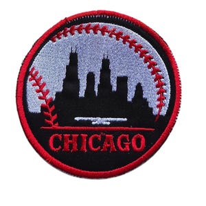 May include: A circular embroidered patch featuring a black silhouette of the Chicago skyline against a light blue background. A red baseball stitch pattern curves along the right side, and the word CHICAGO is stitched in red at the bottom.