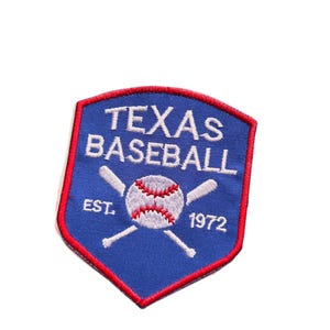 Op de afbeelding: Een blauw, rood en wit honkbalpatch met de witte woorden "TEXAS BASEBALL". Een honkbal en gekruiste knuppels staan in het midden. De tekst "EST. 1972" is ook opgenomen. De patch heeft een schildvorm.