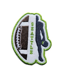May include: Green and white embroidered patch with a silhouette of a football player holding a football and the word "SEATTLE" on the side.