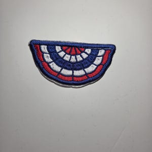 May include: A semi-circular embroidered patch featuring a pleated bunting design in red, white, and blue. The patch has a thick dark blue border and a repeating pattern of alternating red and white segments arranged in a fan-like shape.