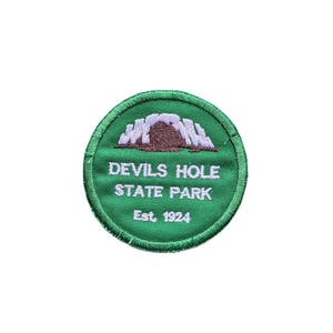 May include: A circular embroidered patch with a green background and a stitched border. The design features a brown and white rock formation graphic above the white text that reads Devils Hole State Park and the establishment date Est. 1924.