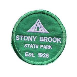 May include: A circular green embroidered patch featuring a white tent icon at the top. The text reads STONY BROOK STATE PARK in white capital letters, followed by Est. 1925 in white text. The patch has a stitched border in a matching green thread.