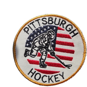 May include: Embroidered patch featuring a hockey player in action, set against a stylized American flag design. The patch is circular, with the words "PITTSBURGH HOCKEY" in a curved layout around the edge. The border is gold.