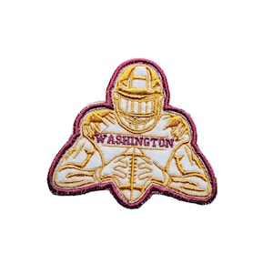 May include: An embroidered patch featuring a football player in a gold uniform with the word "WASHINGTON" across the chest. The patch has a maroon border.