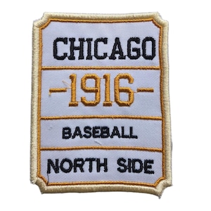May include: A rectangular embroidered patch with a white background and a gold border. The text reads CHICAGO in black, 1916 in gold, BASEBALL in black, and NORTH SIDE in black. The design is divided into three horizontal sections by gold lines.