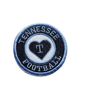 May include: A blue and white embroidered patch with the words "Tennessee Football" surrounding a white heart with a blue "T" inside.
