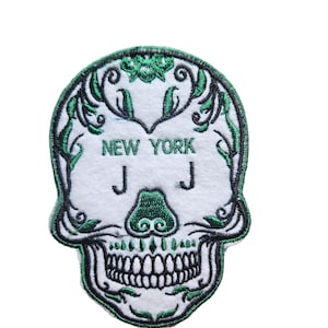 May include: Green embroidered skull patch with the words "NEW YORK" and "JJ" inside the skull. The skull has a floral design around the edges.