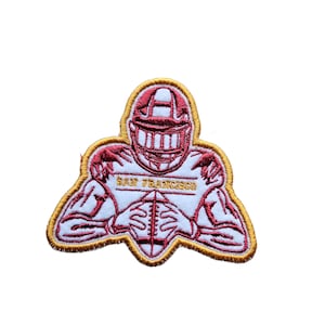 May include: Embroidered patch featuring a red and white football player in a helmet, holding a football. The player is wearing a jersey with the text "SAN FRANCISCO" on it. The patch has a gold outline.