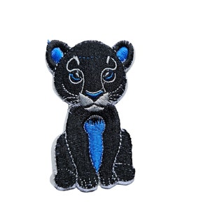 Op de afbeelding: Zwarte en blauwe geborduurde strijkpatch van een cartoon-panterwelpje dat met gekruiste pootjes zit.