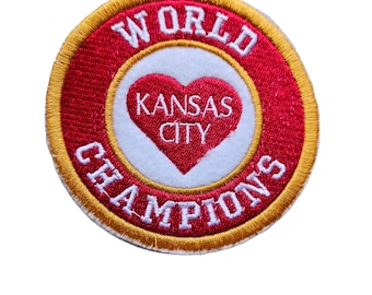 Puede incluir: Un parche bordado en rojo y dorado con las palabras "World Champions" alrededor de un círculo blanco que contiene un corazón rojo que dice "Kansas City".