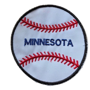Può includere: Una toppa ricamata circolare che presenta un design a forma di palla da baseball bianca con dettagli di cuciture rosse. La parola MINNESOTA è ricamata in lettere maiuscole blu al centro della toppa, rifinita con un bordo cucito nero.