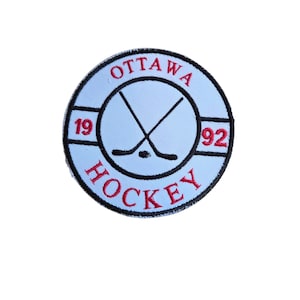 Puede incluir: Un parche circular con fondo azul claro y borde negro. El parche presenta la palabra "OTTAWA" en rojo, arqueada en la parte superior, y "HOCKEY" en rojo, arqueada en la parte inferior. Palos de hockey cruzados y un disco en el centro. Los números "19" y "92" están a ambos lados.