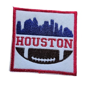 Op de afbeelding: Rode, witte en blauwe geborduurde patch met een skyline van Houston, Texas en een voetbal in het midden. De tekst "HOUSTON" is geborduurd in rood.