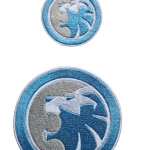 May include: Two embroidered patches featuring a blue lion's head with white details inside a grey circle with a blue outer ring.