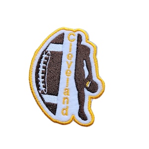 May include: An embroidered patch featuring a brown football and a brown silhouette of a football player. The word "Cleveland" is written vertically in yellow on the patch.
