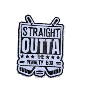 Op de afbeelding: Witte en zwarte geborduurde patch met de tekst "Straight Outta The Penalty Box" en twee gekruiste hockeysticks.