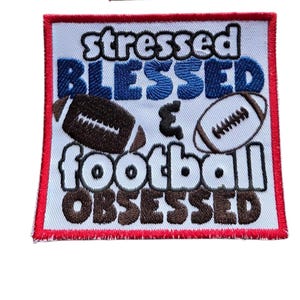 May include: Embroidered patch with the words "stressed BLESSED & football OBSESSED" in black, blue, and brown. Two footballs are also embroidered on the patch. The patch has a white background with a red border.