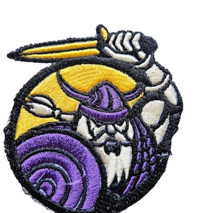 May include: Embroidered patch depicting a cartoon Viking warrior holding a sword and shield. The warrior is wearing a purple helmet and has a white beard. The background is yellow and purple.