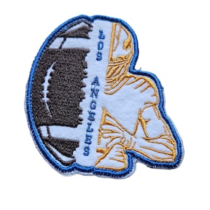 Peut inclure: Un patch brodé représentant un ballon de football et un joueur de football en position agenouillée. Le patch est bordé de bleu et porte le texte "405 ANGELES".