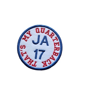 Puede incluir: Un parche circular blanco con bordado azul y rojo. El texto dice "That's My Quarterback JA 17".